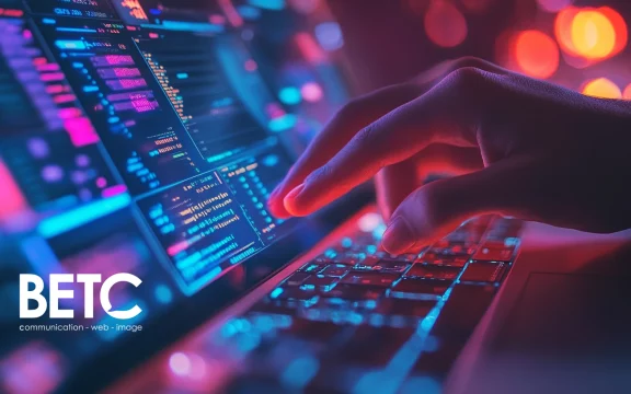Main tapant sur un clavier illuminé, représentant le travail numérique dans une agence digitale.