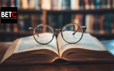 Des lunettes posées sur un livre ouvert dans une bibliothèque, logo BETC communication en arrière-plan.